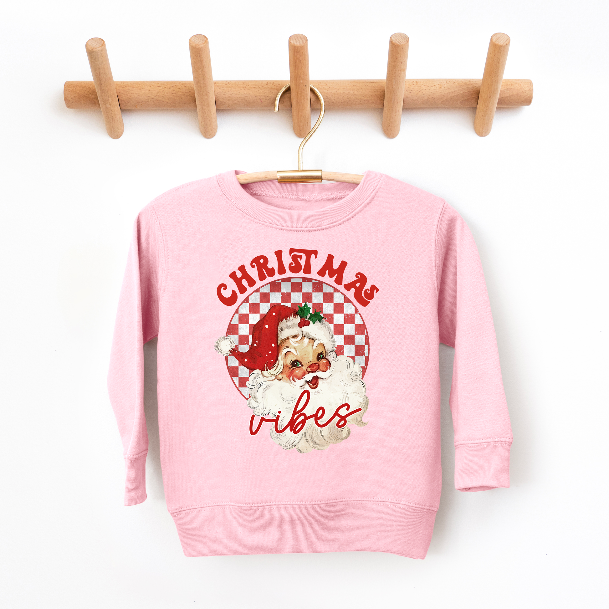 Pink sweatshirt with Christmas design on a wooden hanger against a white background