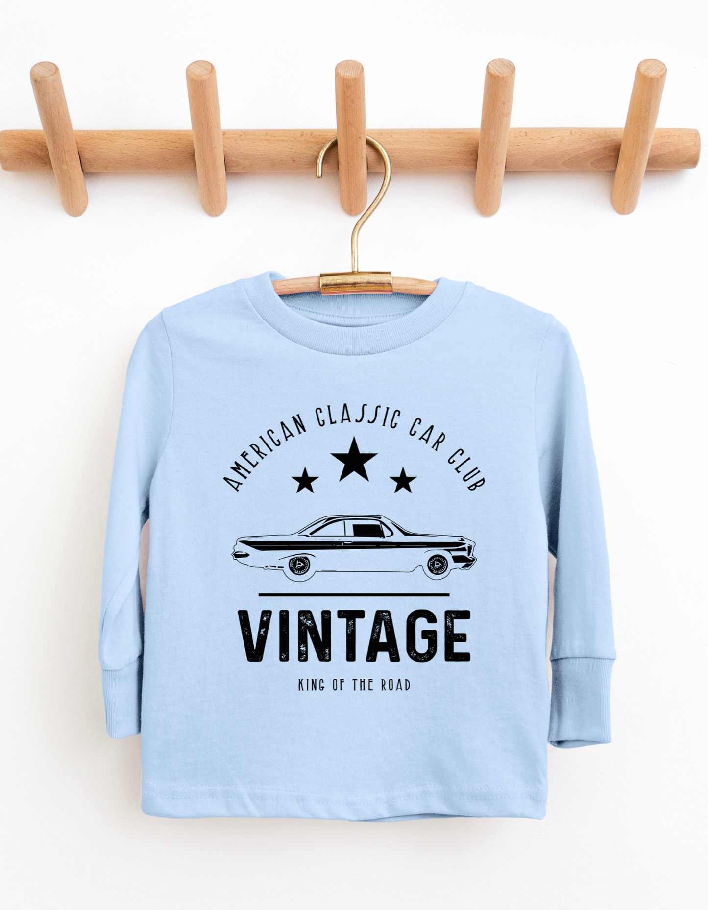 Light blue long-sleeve shirt with vintage car design on a wooden hanger against a white background