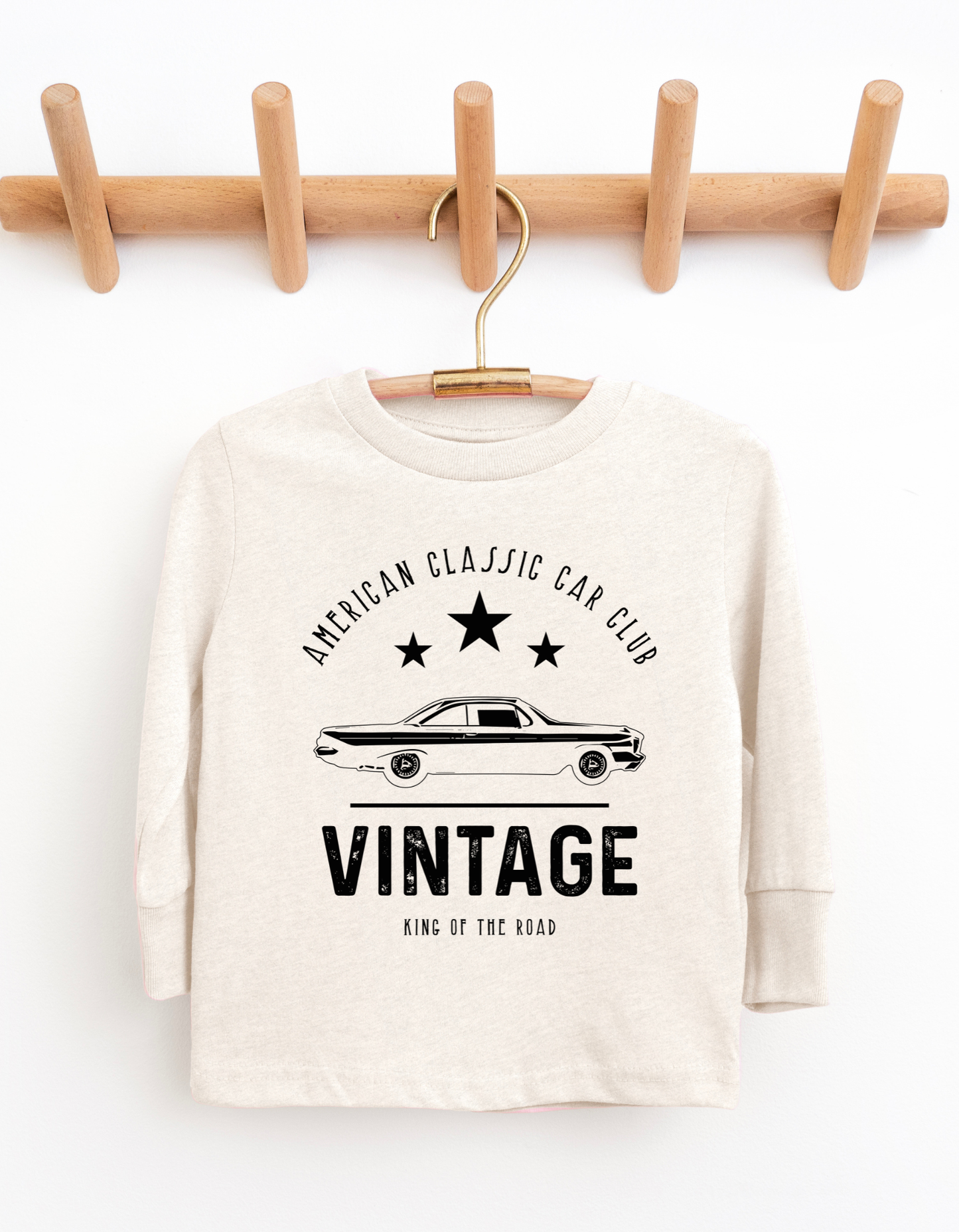 White sweatshirt with vintage car design and text on a wooden hanger against a white background