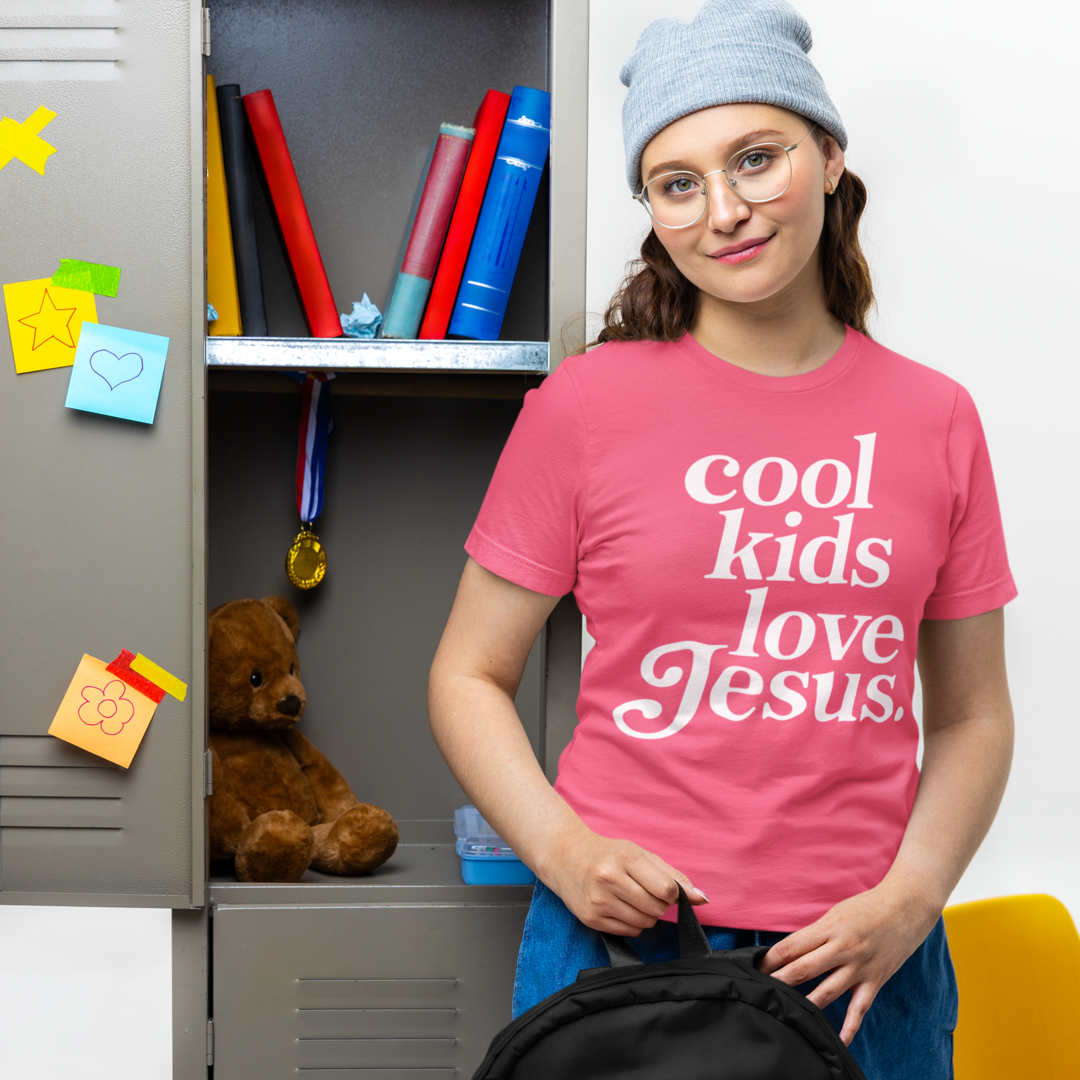 Person wearing a pink 'cool kids love Jesus' t-shirt standing next to an open locker with school supplies.