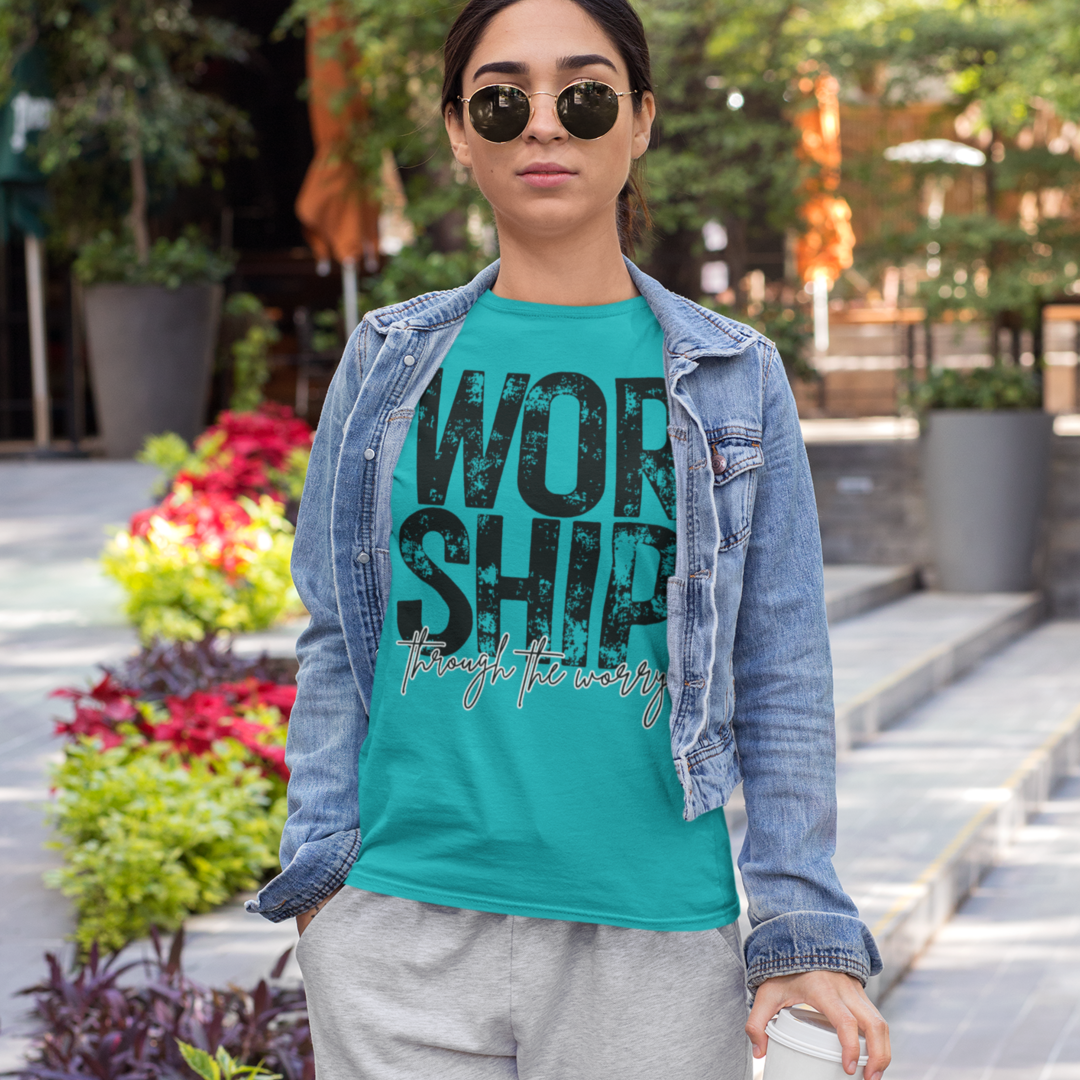 Person wearing a teal t-shirt with 'Worship through the worry' text, standing outdoors.