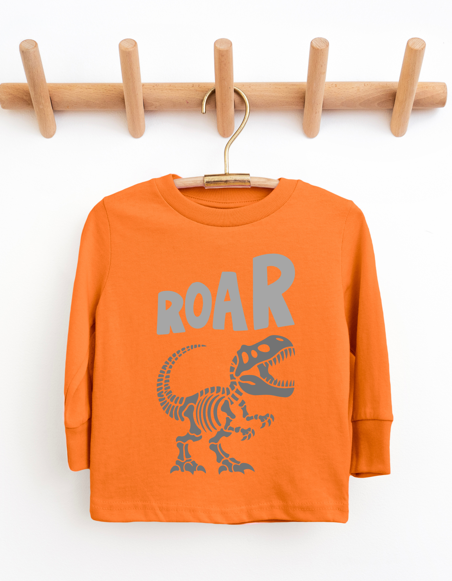 Orange long-sleeve shirt with dinosaur graphic and 'ROAR' text on a wooden hanger against a white background