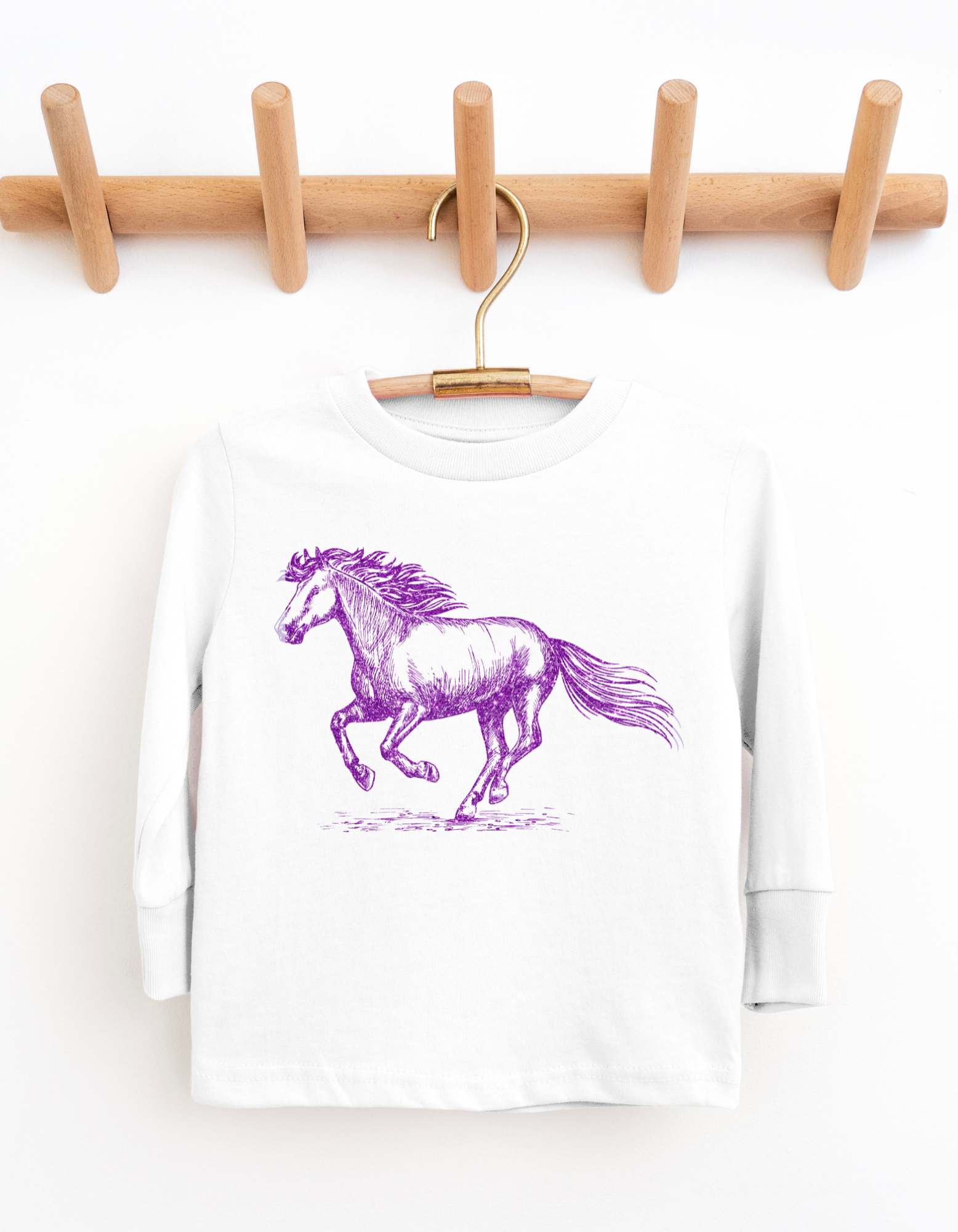 White long-sleeve shirt with a purple horse graphic on a wooden hanger against a white background