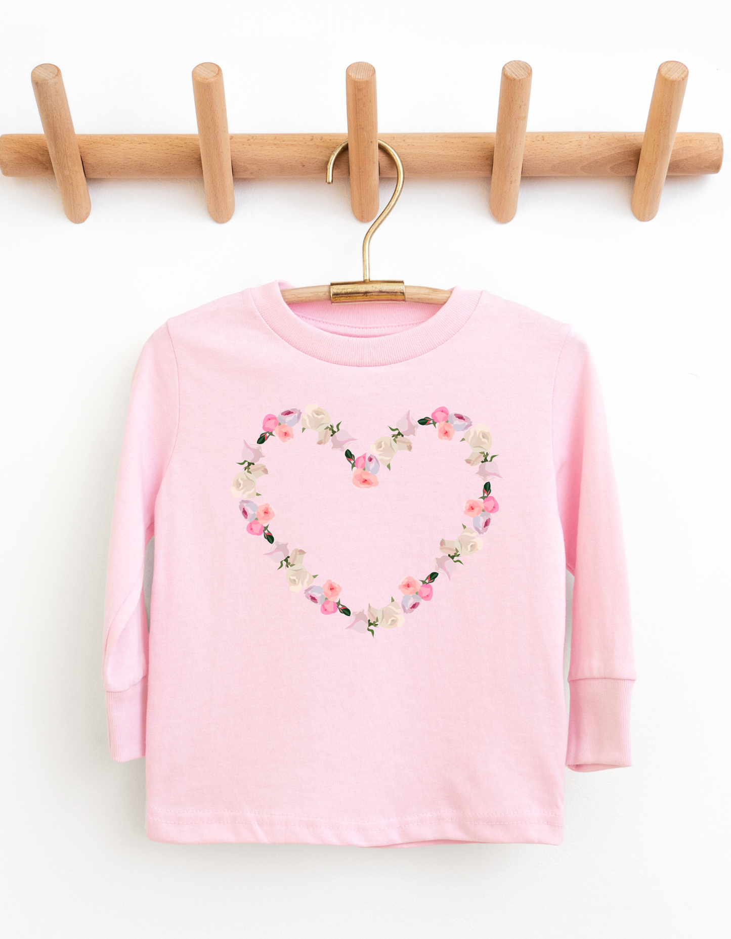 Pink long-sleeve shirt with floral heart design on a wooden hanger against a white background