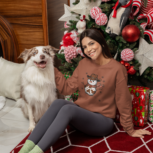 Woman wearing a sweater with a snowman design sitting next to a dog in front of a decorated Christmas tree.
