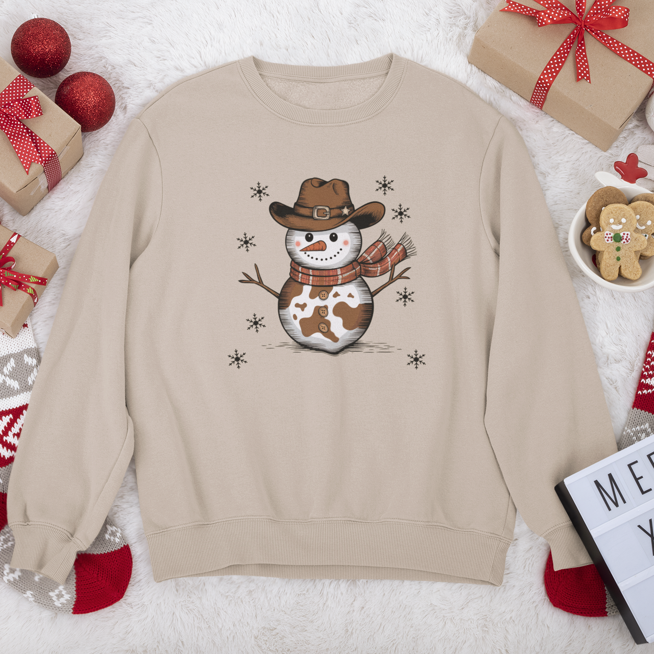 Beige sweatshirt with a snowman design wearing a cowboy hat and scarf, surrounded by Christmas decorations.