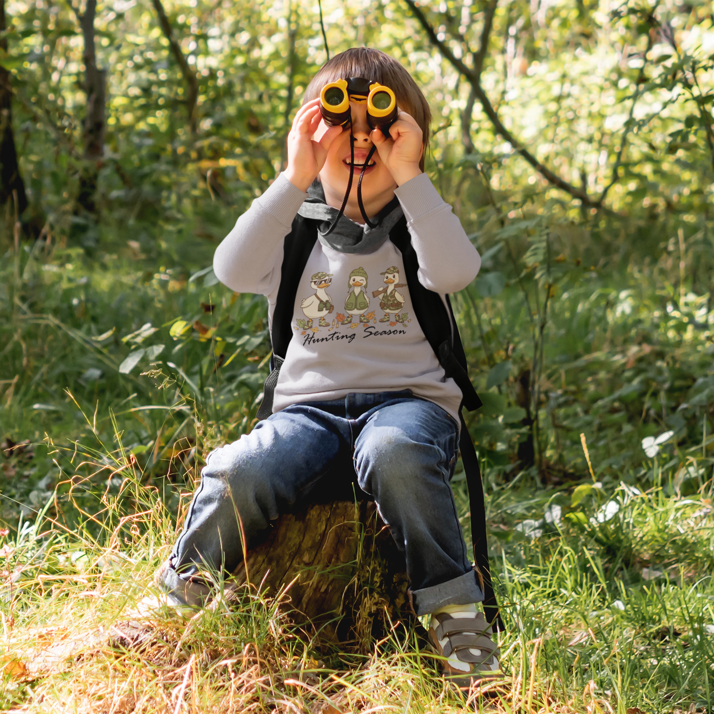 Child in a forest setting with binoculars, wearing a shirt with cartoon characters.