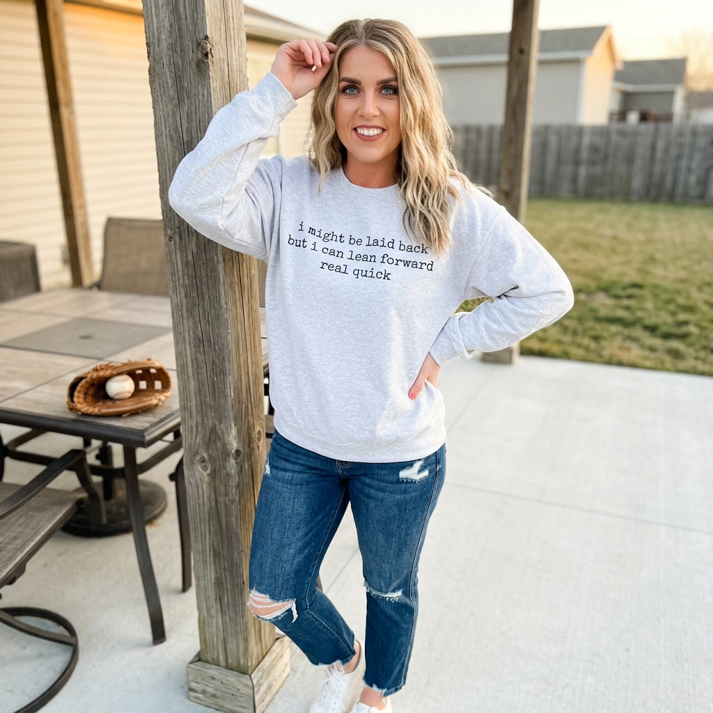 Woman wearing a light gray sweatshirt with text and blue jeans, standing outdoors.