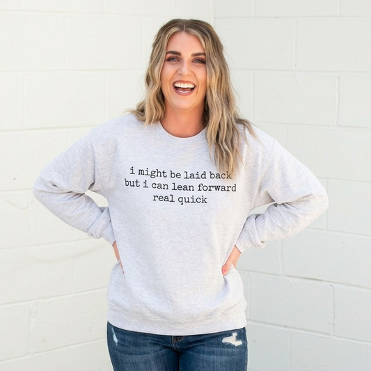Woman wearing a gray sweatshirt with text and blue jeans against a white wall.
