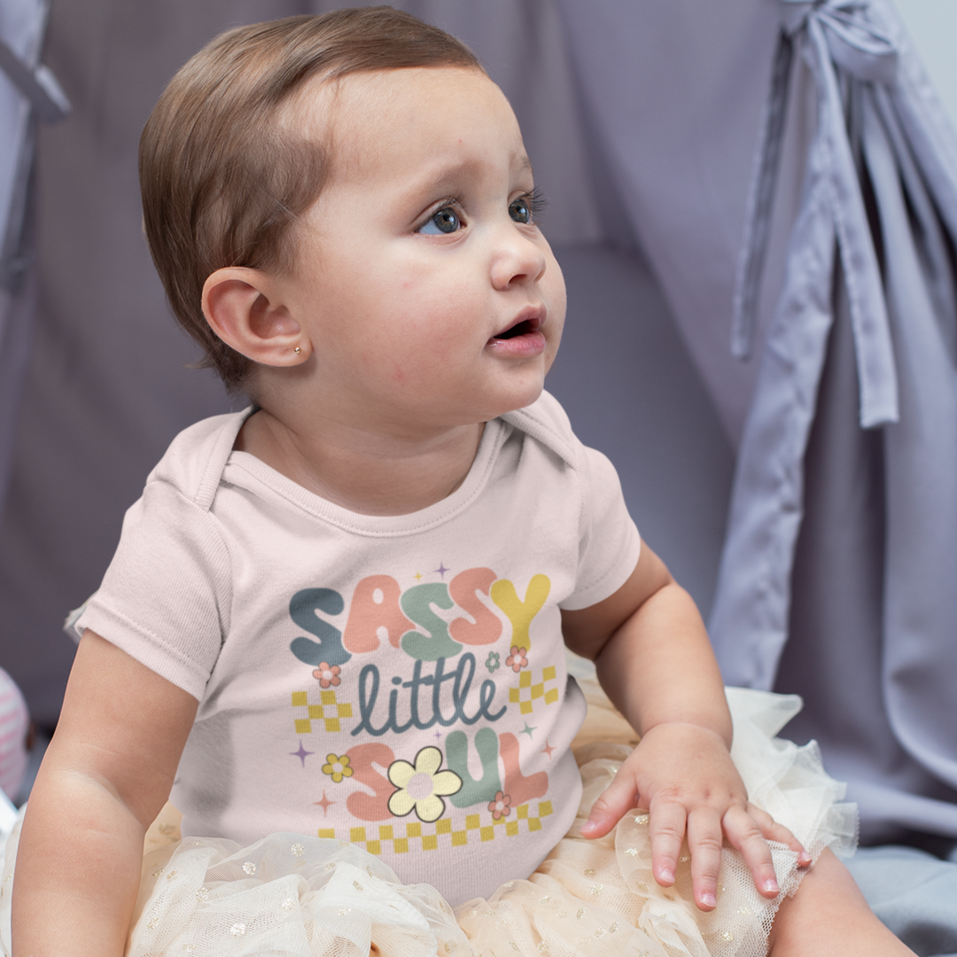 A toddler wearing a pink bodysuit with the text 'SASSY LITTLE SOUL' printed on the front.