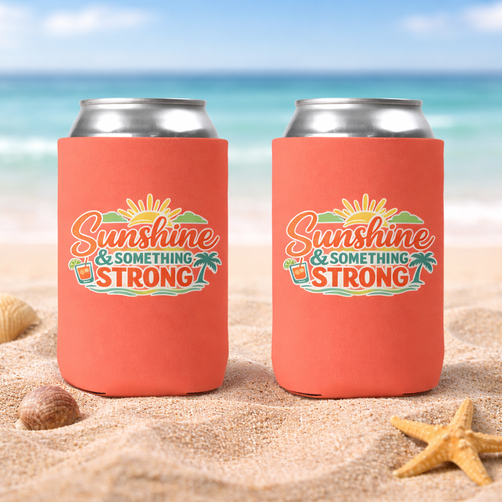 Two coral can coolers with 'Sunshine & Something Strong' text on a beach background.