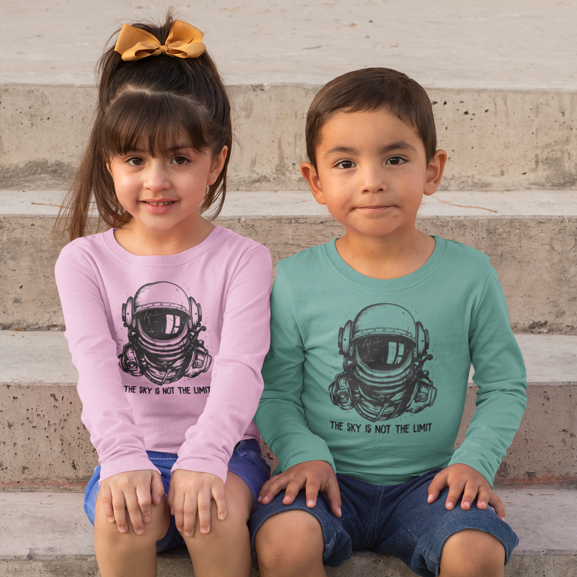 Two children wearing shirts with astronaut graphics on a stone step background