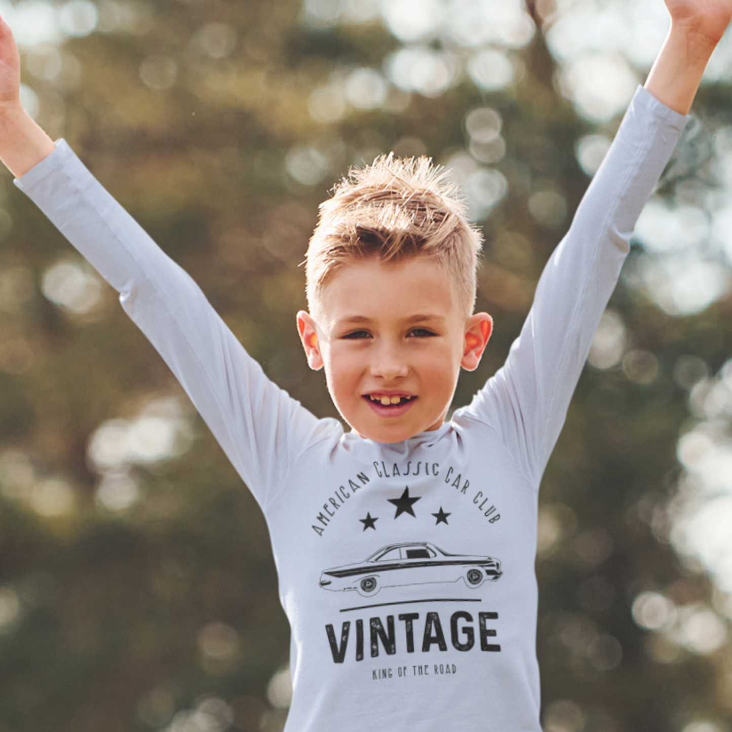 Child wearing a 'Vintage' t-shirt with raised arms against a blurred natural background