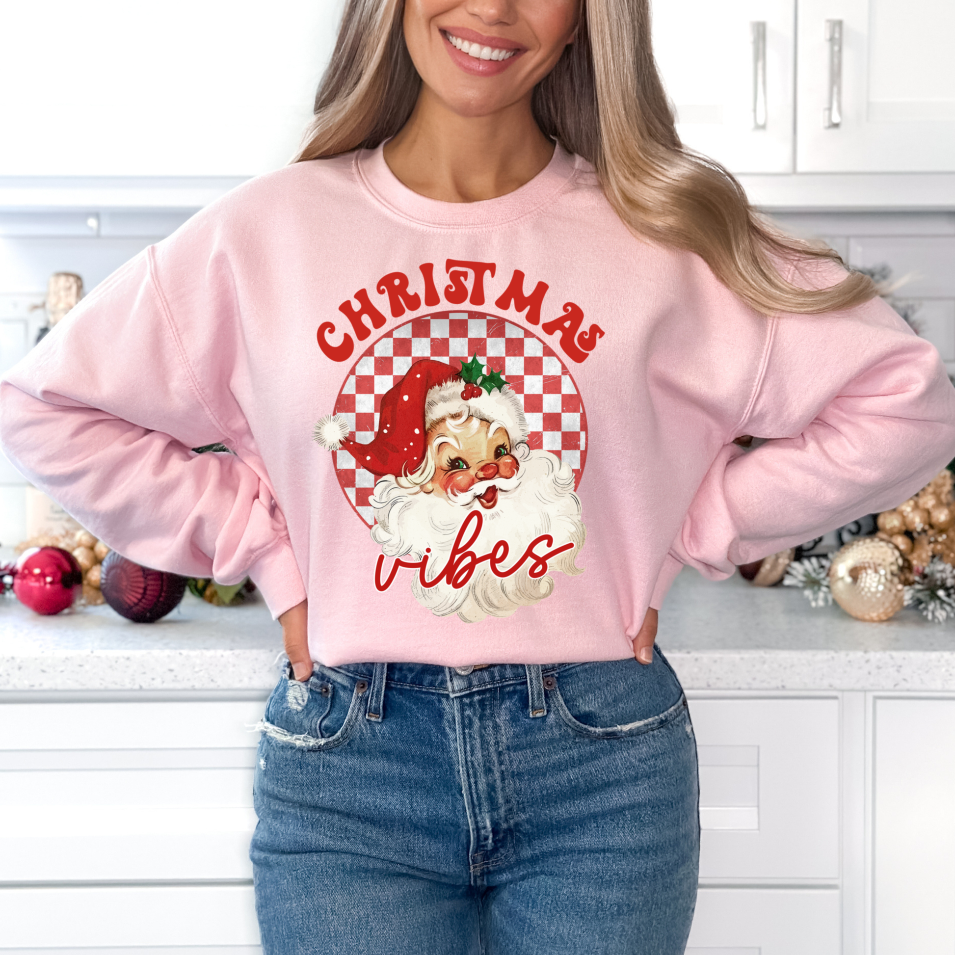 Person wearing a pink sweatshirt with Santa Claus graphic and 'Christmas vibes' text in a kitchen setting.