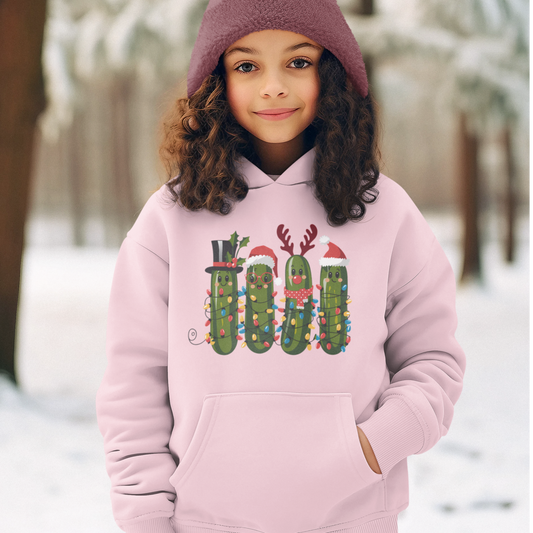 A girl wearing a light pink hoodie with a Christmas pickle graphic, featuring four festive pickles decorated with Santa hats, reindeer antlers, and holiday lights.