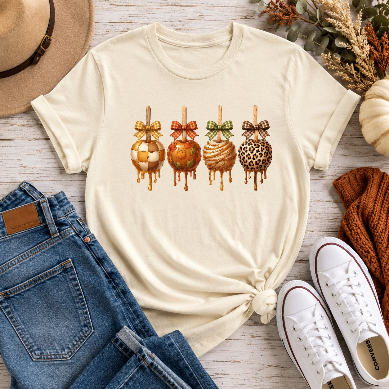 Tea-Shirt Shoppe cream graphic tee featuring four decorated caramel apples with plaid bows for a cozy fall aesthetic.