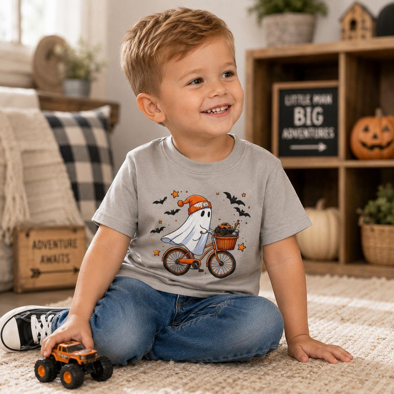 A smiling toddler wearing a Tea-Shirt Shoppe heather gray graphic tee featuring a ghost on a bicycle with toy trucks.