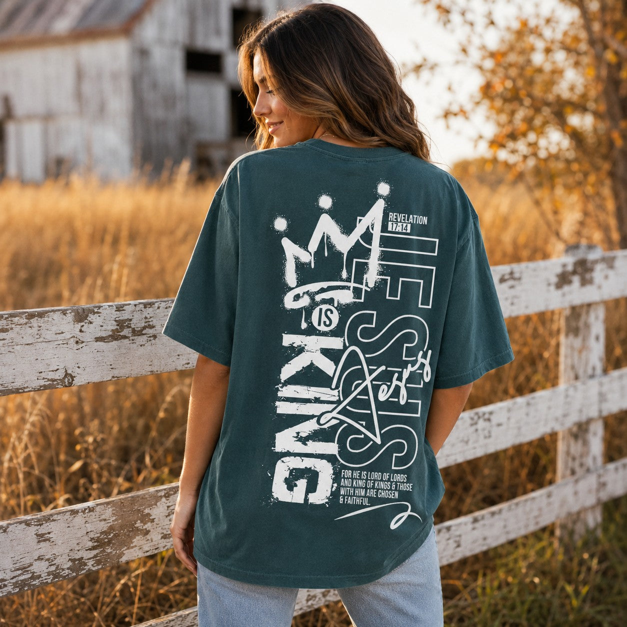 Tea-Shirt Shoppe unisex graphic tee in dark green with Jesus Is King crown design on back, worn by a woman outdoors.