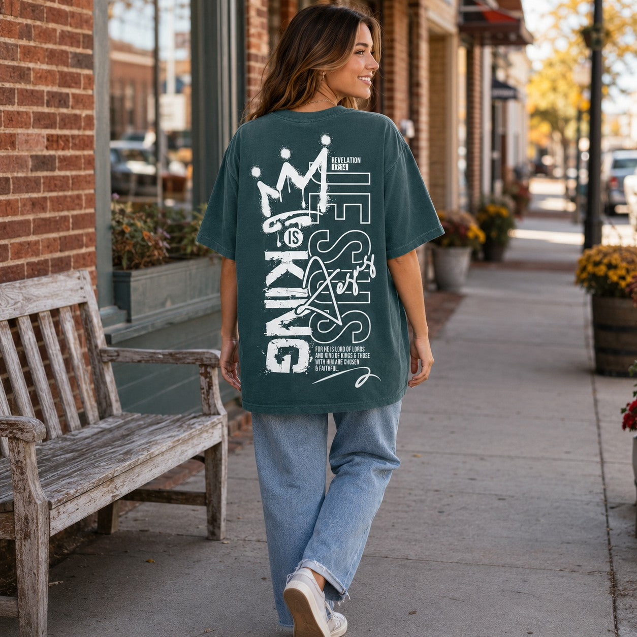 Tea-Shirt Shoppe dark green unisex graphic tee with Jesus Is King crown design on back worn by a woman on a sidewalk