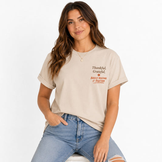 Woman wearing a beige Tea Shirt Shoppe Wholesale graphic tee with Thankful Grateful Barely Holding it together text