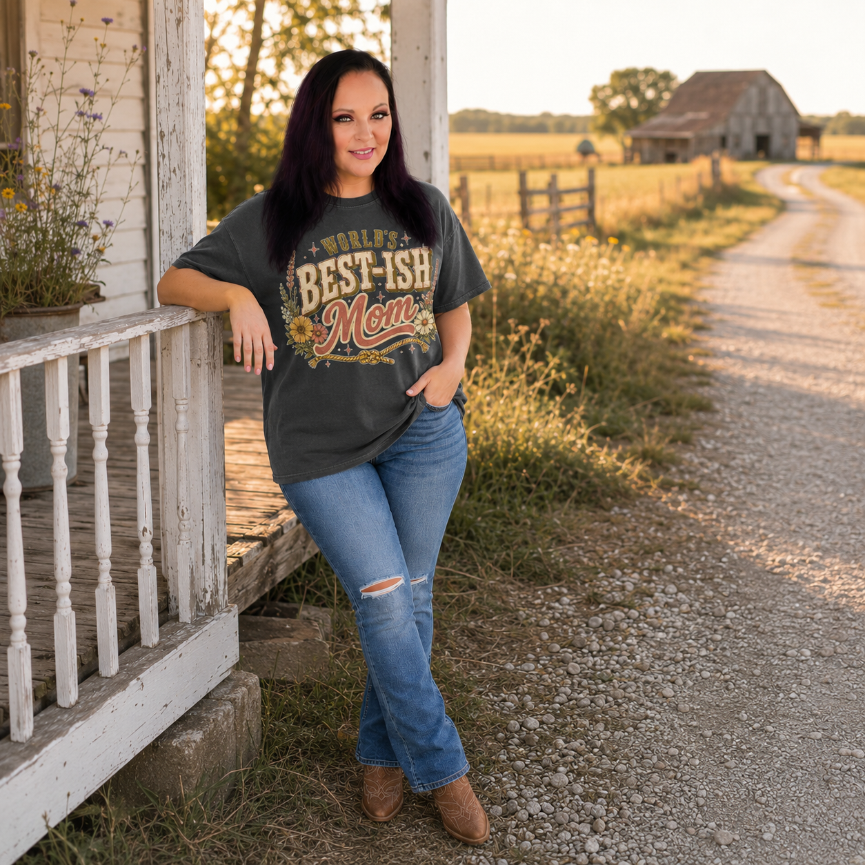 Tea Shirt Shoppe Wholesale charcoal graphic tee with Worlds Best-Ish Mom print, worn by a woman on a rustic porch.