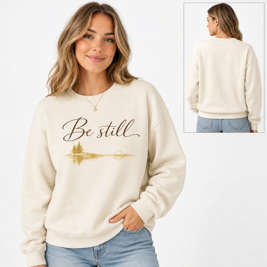 Tea Shirt Shoppe Wholesale cream crewneck sweatshirt with Be Still graphic and lakeside sunset print on a smiling woman