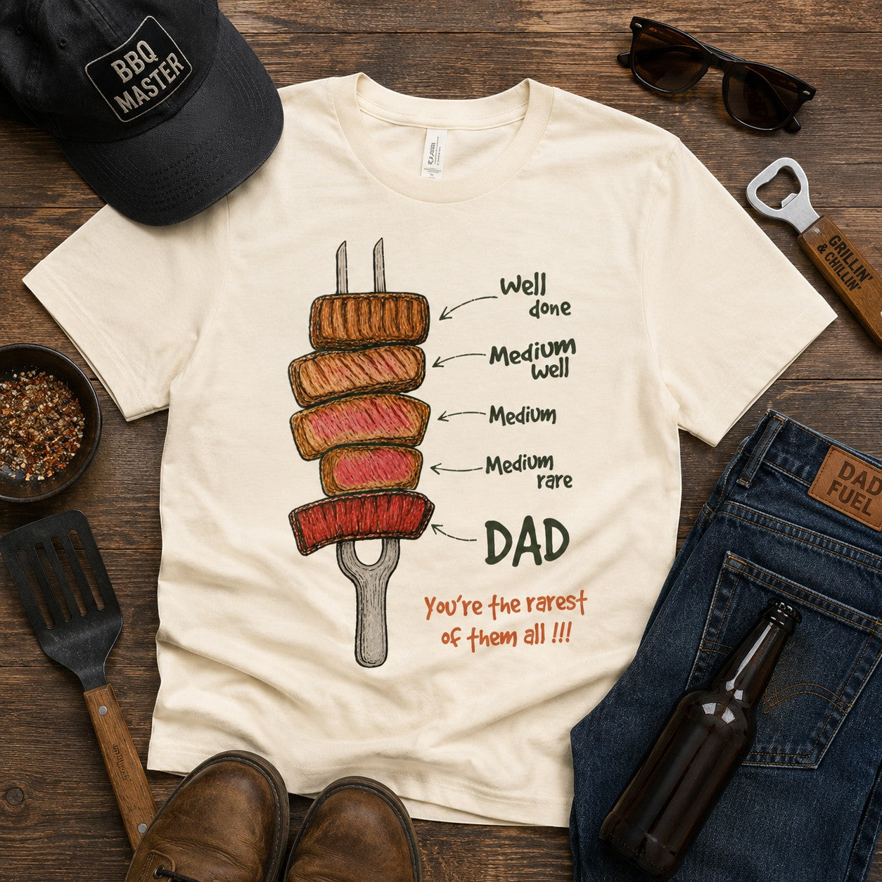Tea Shirt Shoppe Wholesale cream graphic tee with steak doneness levels labeled Well Done to Medium Rare, with DAD and "You're the rarest of them all!!!" text.