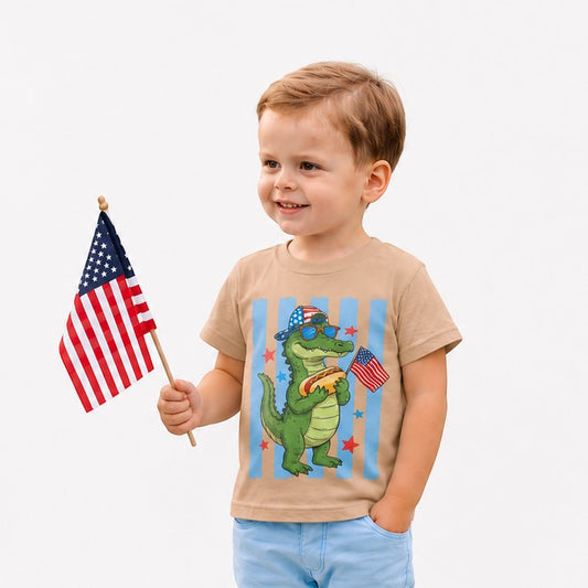 Tea Shirt Shoppe Wholesale tan 100% cotton youth graphic tee with a cartoon alligator holding a hot dog and American flags.