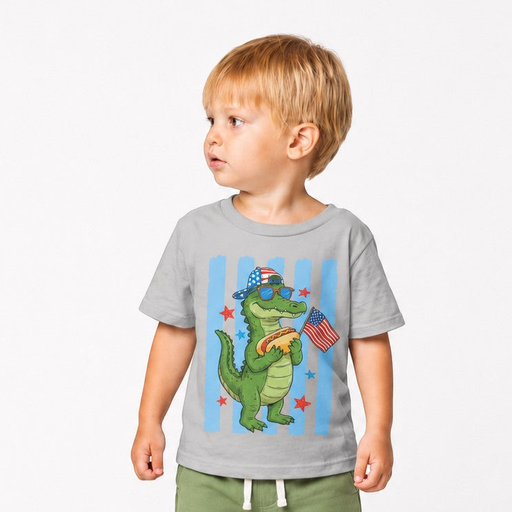 Tea Shirt Shoppe Wholesale grey 100% cotton youth graphic tee with a cartoon alligator wearing sunglasses and a flag hat, holding a hot dog and an American flag.