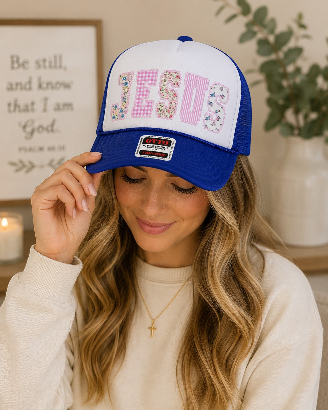 Tea Shirt Shoppe Wholesale blue trucker hat with white front panel featuring "JESUS" in patchwork floral and gingham letters.