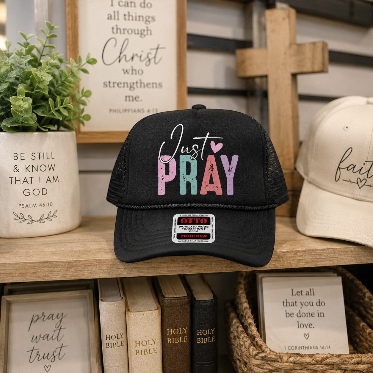 Tea Shirt Shoppe Wholesale black trucker hat with Just Pray graphic in distressed pastel lettering and mesh back.