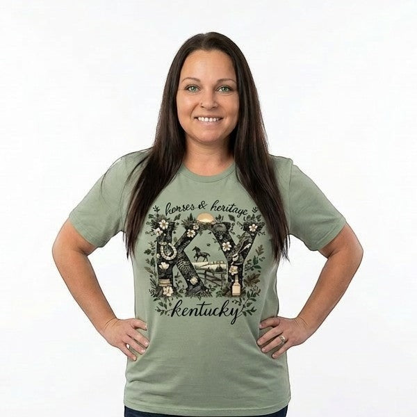 Tea Shirt Shoppe Wholesale sage green graphic tee with "KY" design featuring horses, fences, and floral elements. Text reads "horses & heritage Kentucky".
