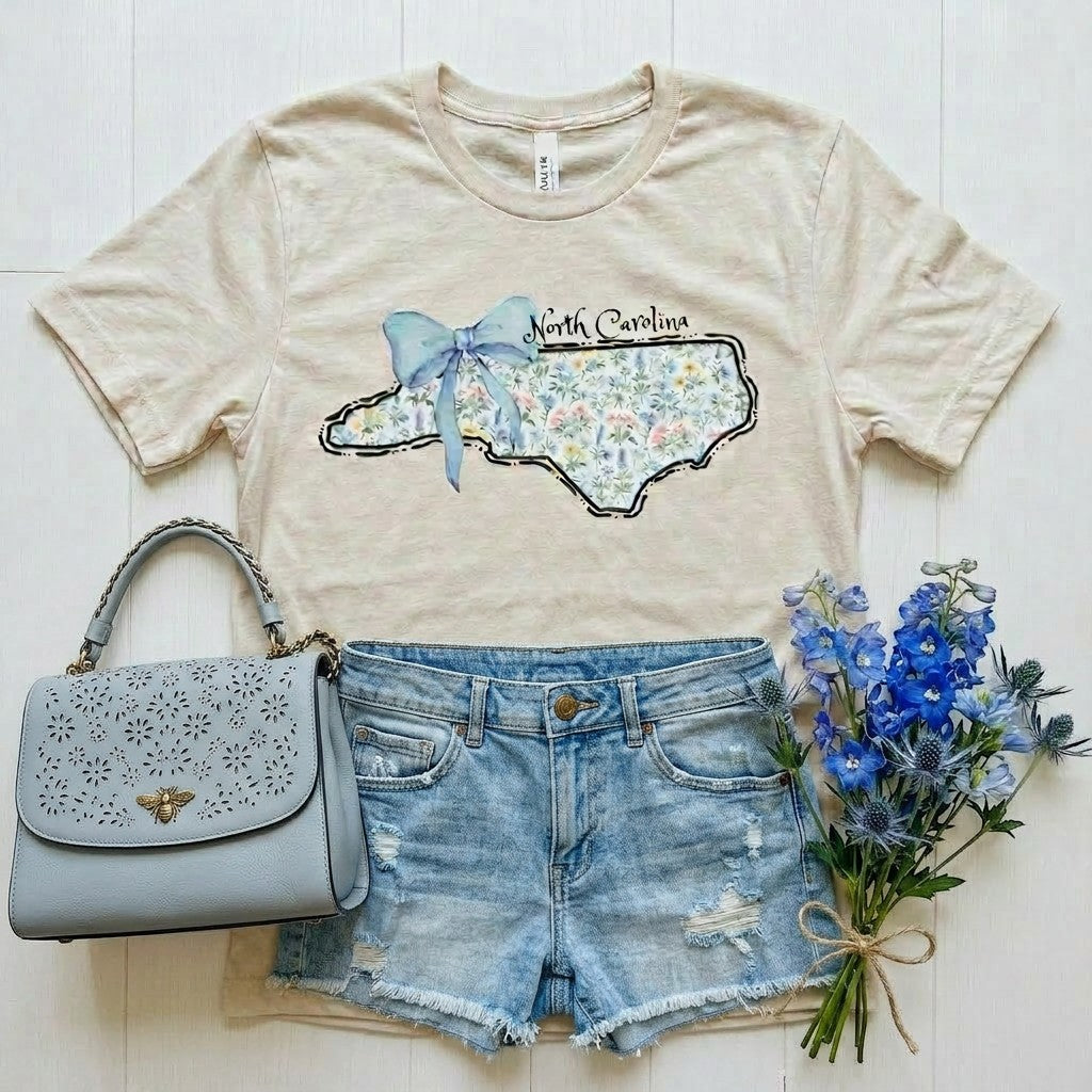 Tea Shirt Shoppe Wholesale light beige graphic t-shirt with North Carolina outline filled with floral pattern and blue bow.