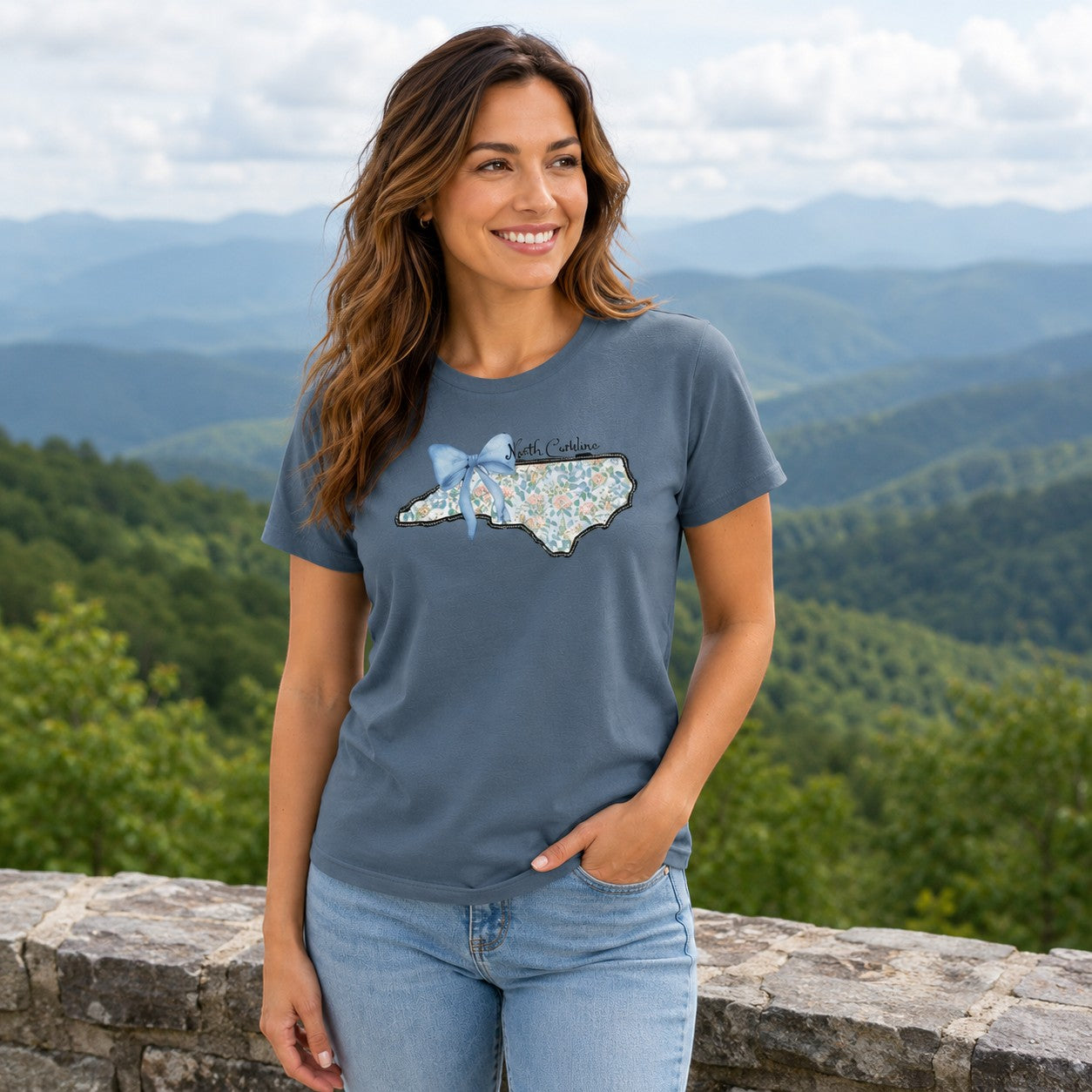Tea Shirt Shoppe Wholesale blue graphic tee with a floral North Carolina state outline and blue bow, worn by a woman.