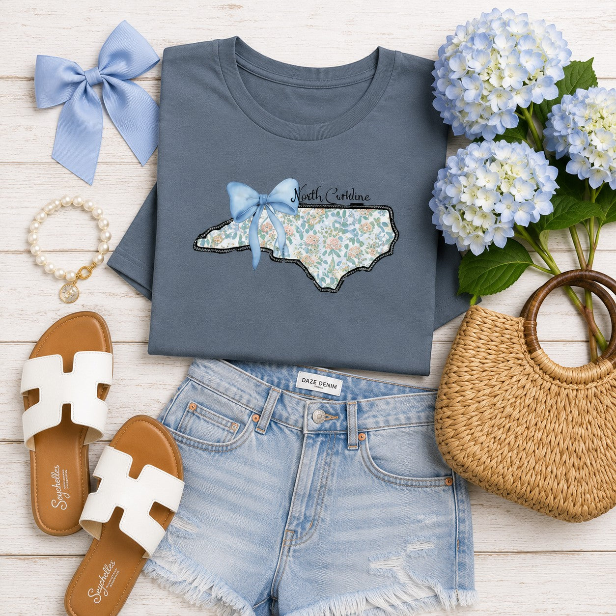 Tea Shirt Shoppe Wholesale blue graphic tee featuring a floral North Carolina state outline with a blue bow accent.