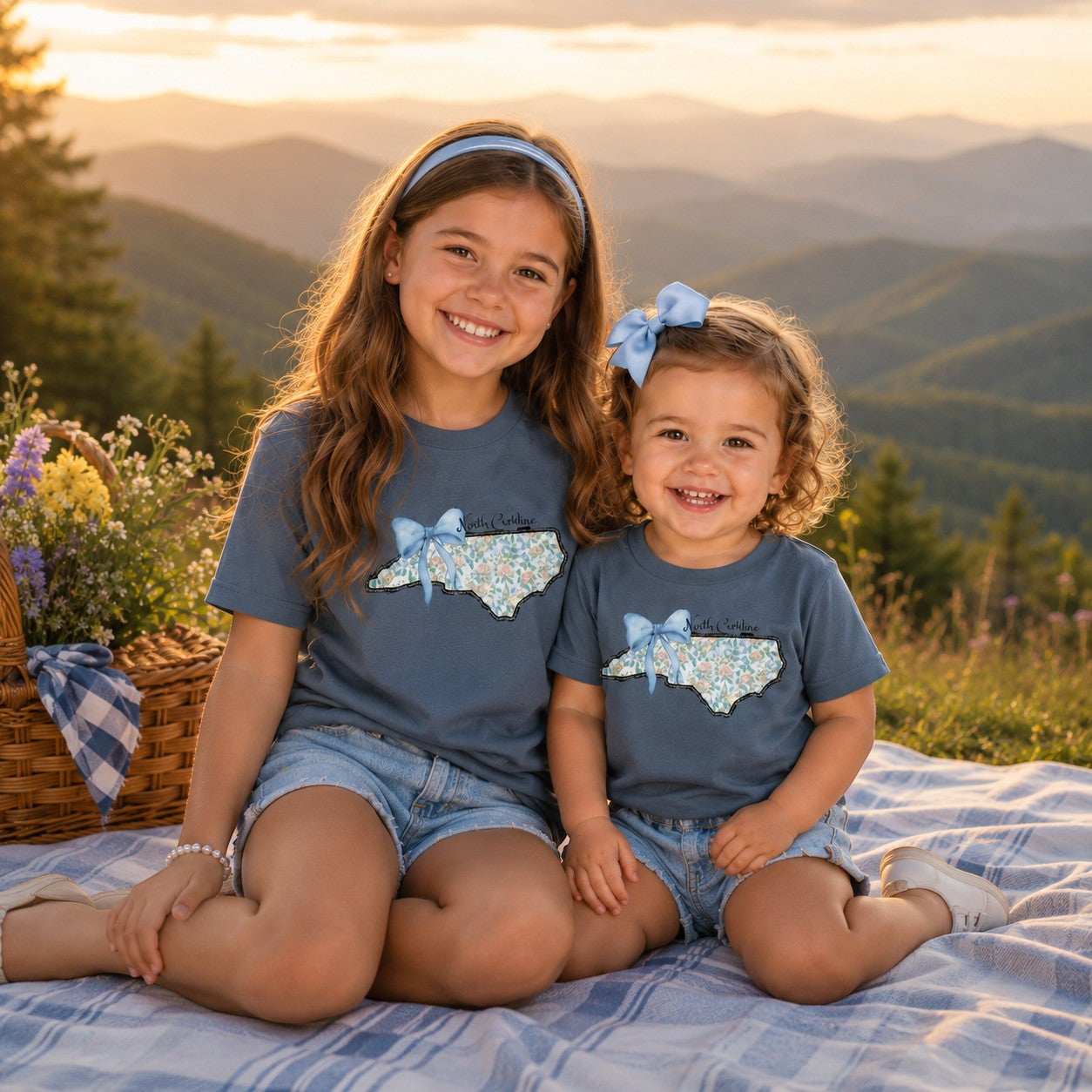 Two girls wearing Tea Shirt Shoppe Wholesale indigo cotton t-shirts with a floral North Carolina state graphic print.