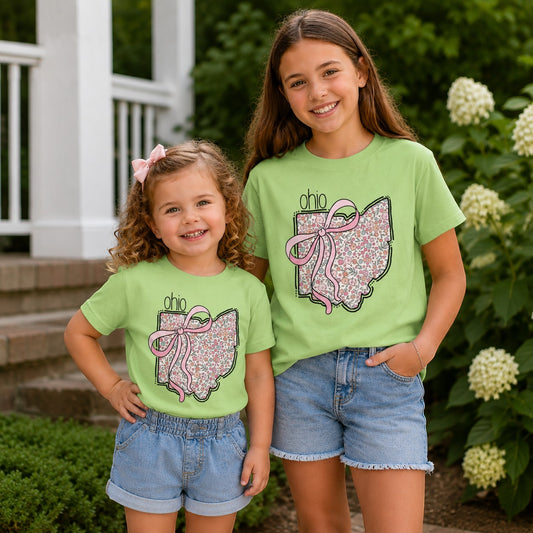 Two girls wearing light green Tea Shirt Shoppe Wholesale t-shirts with a floral Ohio state outline and pink bow graphic