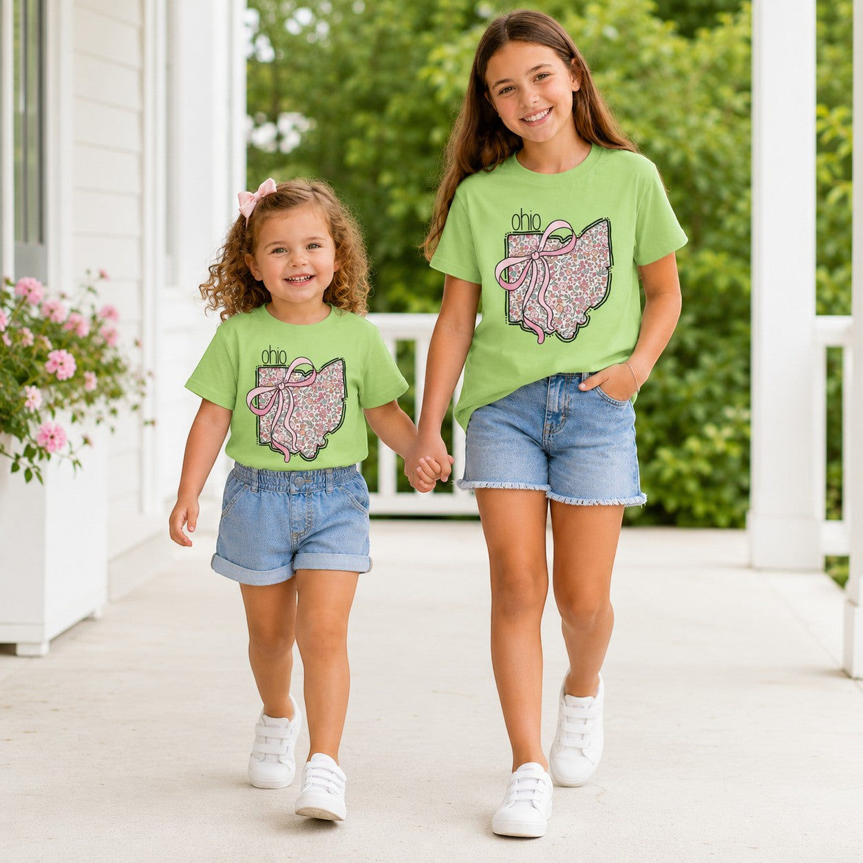 Two girls wearing Tea Shirt Shoppe Wholesale light green Ohio floral graphic t-shirts with pink bows on a porch.