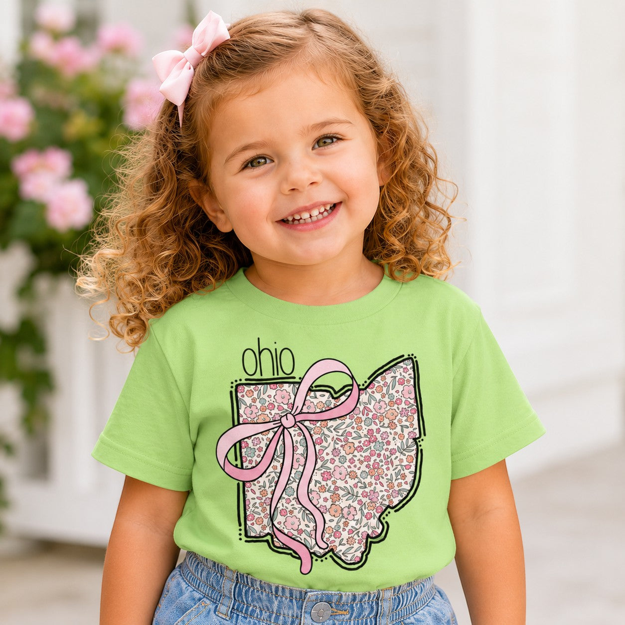 Tea Shirt Shoppe Wholesale light green t-shirt with Ohio state floral graphic and pink bow worn by a smiling girl.