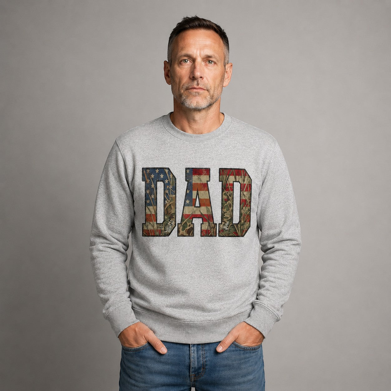 Tea Shirt Shoppe Wholesale heather grey crewneck sweatshirt with "DAD" graphic featuring American flag and camouflage patterns.