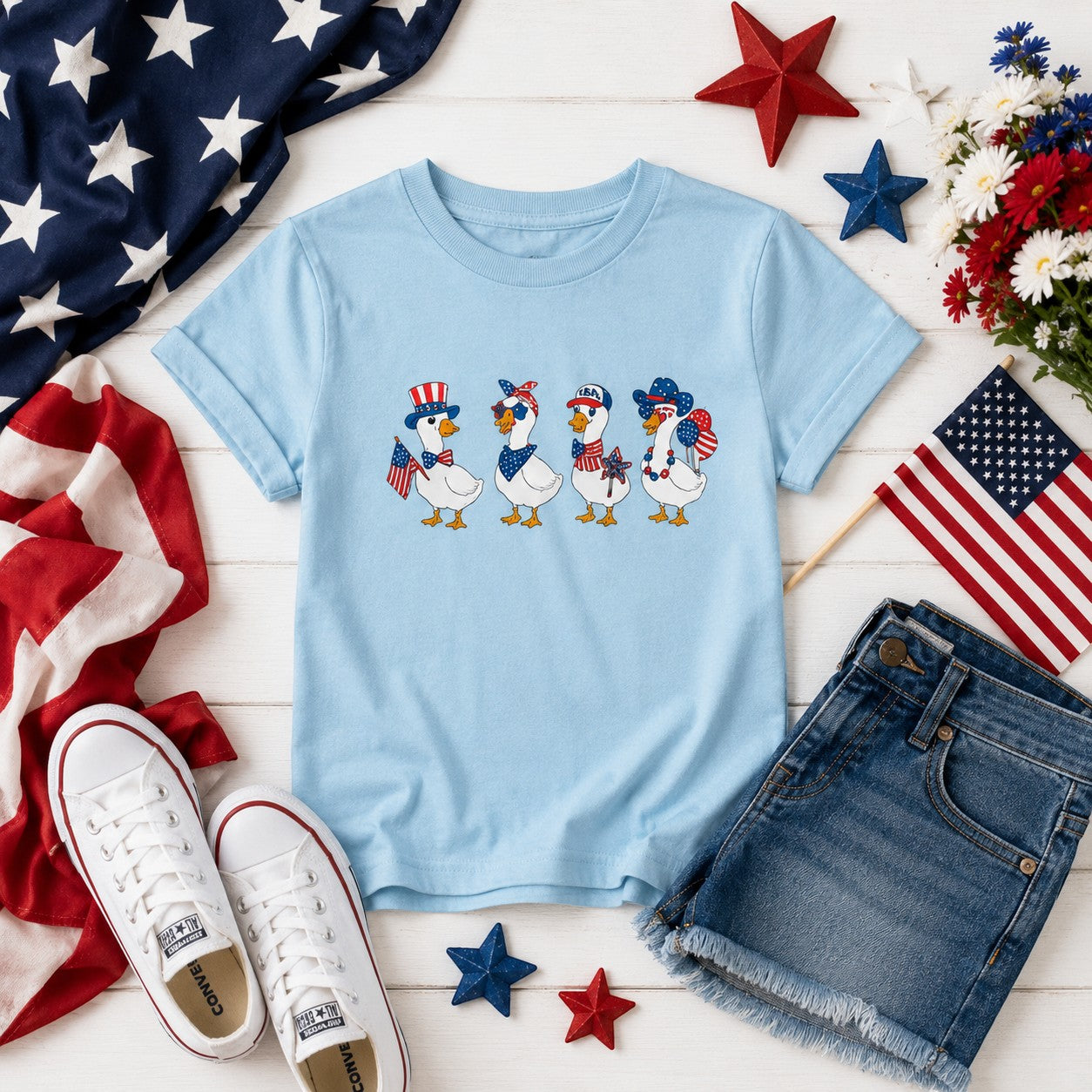 Tea Shirt Shoppe Wholesale light blue graphic tee with four patriotic ducks wearing hats and holding flags.