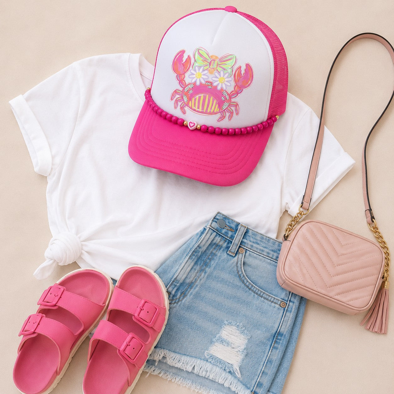 Tea Shirt Shoppe Wholesale pink beaded hat chain on a crab trucker hat with a white t-shirt, denim shorts, and sandals.