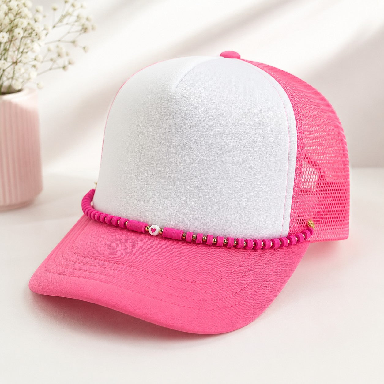Tea Shirt Shoppe Wholesale pink trucker hat with a decorative beaded chain featuring heart and metallic accents.