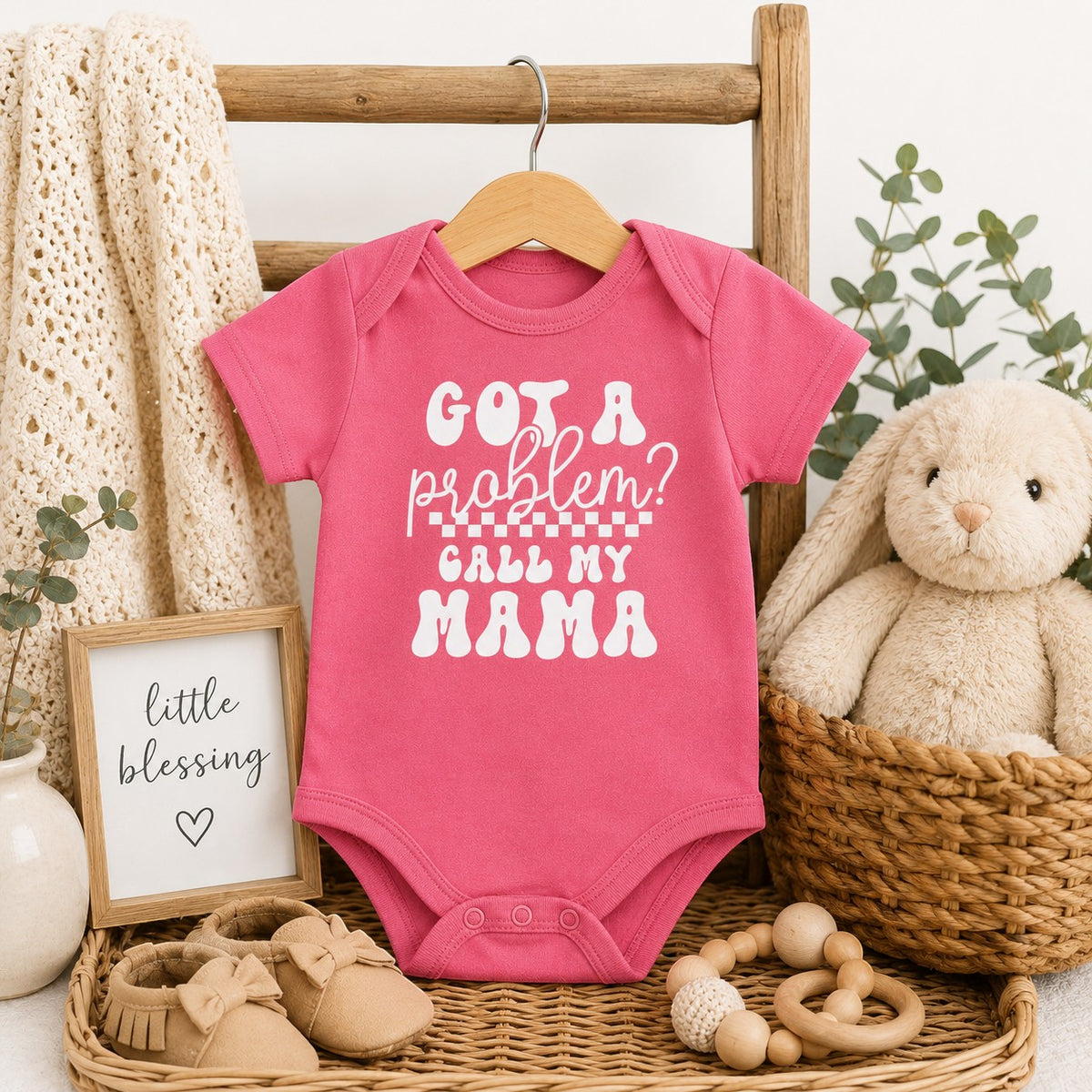 Tea Shirt Shoppe Wholesale pink infant bodysuit with white Got a Problem Call My Mama text on a wooden hanger