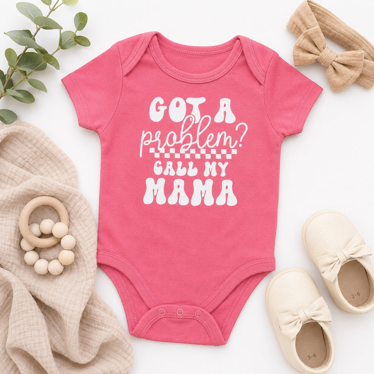 Tea Shirt Shoppe Wholesale pink infant bodysuit with white Got a Problem Call My Mama text, flat lay with baby shoes.