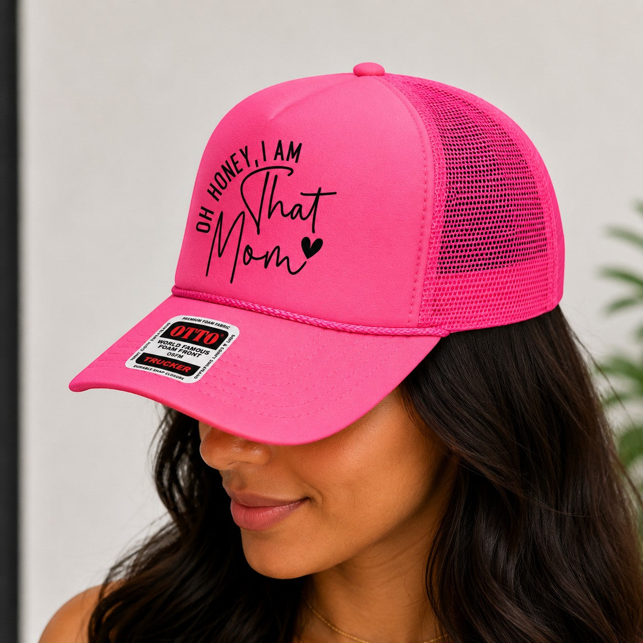 Tea Shirt Shoppe Wholesale bright pink trucker hat with "Oh Honey, I am That Mom" text and black graphic.