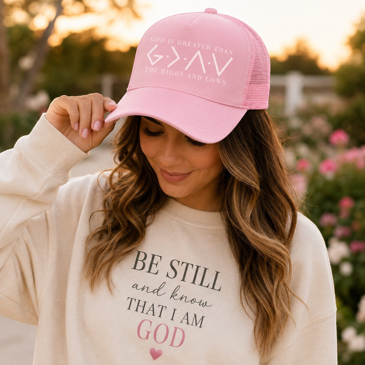 Tea Shirt Shoppe Wholesale pink trucker hat with "God Is Greater Than The Highs And Lows" graphic. Mesh back.