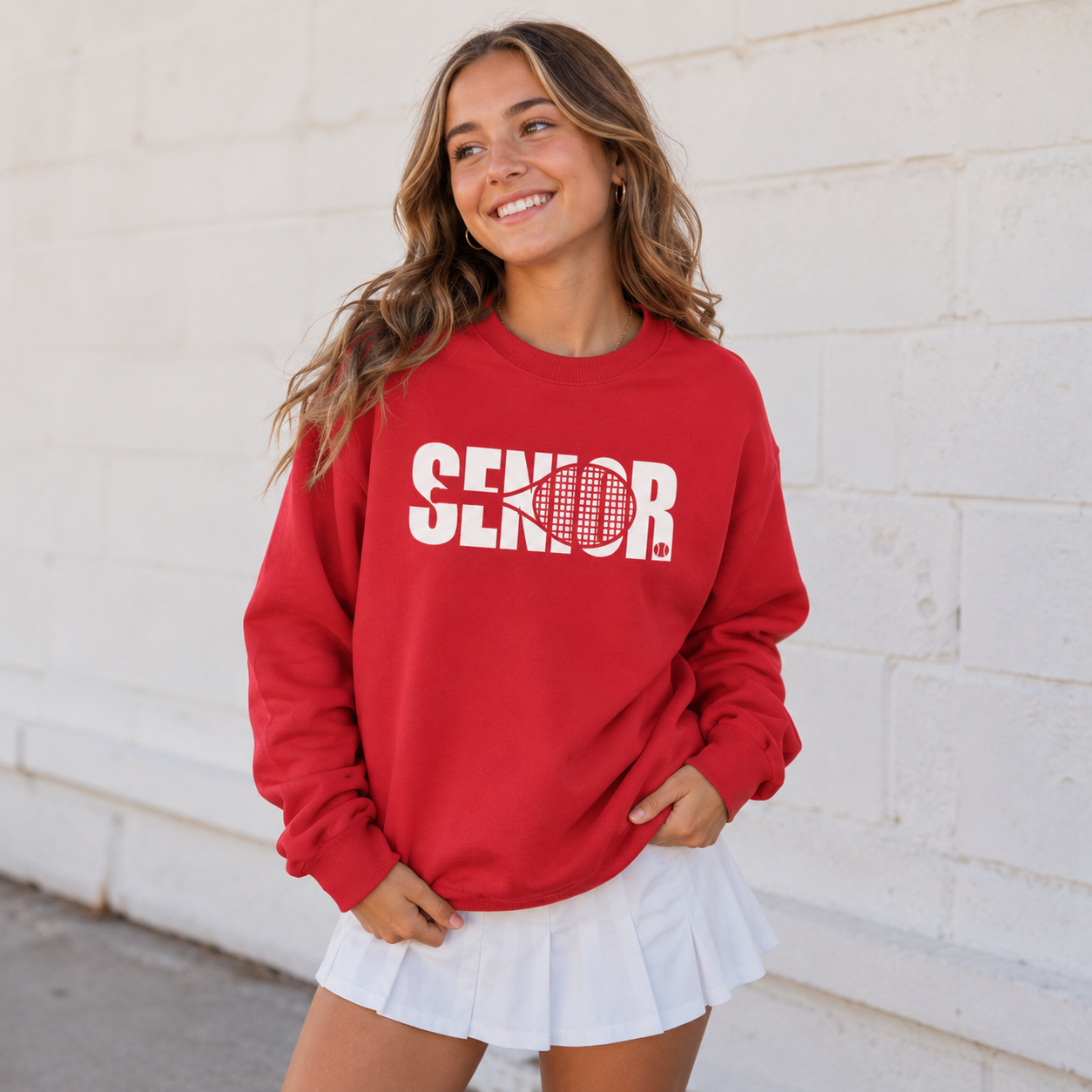 Woman wearing a red Tea Shirt Shoppe Wholesale crewneck sweatshirt with white Senior tennis graphic and white skirt