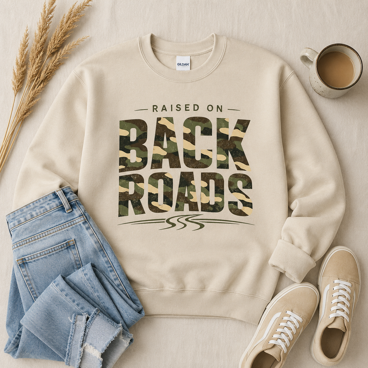 Tea Shirt Shoppe Wholesale sand crewneck sweatshirt with camo Raised On Back Roads graphic, styled with denim and sneakers.